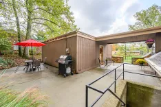 Backyard patio area with outdoor dining set under a red umbrella, a barbecue grill, and surrounding autumn trees.