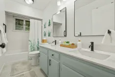 Bright, modern bathroom with a double vanity, subway tiles, large mirrors, bathtub with white curtain, and decorative plants.
