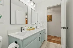 Modern bathroom interior with double sink vanity, large mirrors, white walls, and a painting beside an open door.