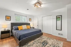 Bright and modern bedroom interior with a navy blue bedspread, yellow accent pillows, hardwood floor, an area rug, and a geometric ceiling light fixture.