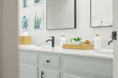 A modern bathroom vanity with a white countertop, black faucet, framed mirrors, and decorative plants.