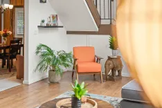 Cozy living room corner with an orange armchair, a potted palm, elephant side table, and a glimpse of a dining area in the background.