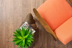 Overhead view of a modern living room corner with a wicker basket containing magazines next to an orange sofa and a green potted plant on a wooden floor.