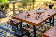 Outdoor wooden dining table and chairs on a porch, scattered with autumn leaves, and a small bowl on the table.