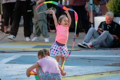 Two children playing with colorful ribbons on a pedestrian street with onlookers in the background.