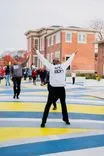 Person celebrating with arms raised on a colorful crosswalk with onlookers in the background.
