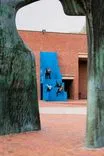 Abstract view of a vibrant blue door through a silhouette of a tree and arched sculpture, creating an artistic composition.