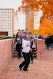 Young people wearing coordinated outfits performing a dance routine on steps outdoors with autumn foliage in the background.