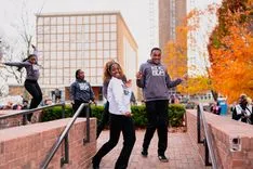 Group of young people dancing and posing on college campus with autumn foliage in the background.