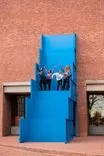 People descending a blue outdoor staircase against a brick building.