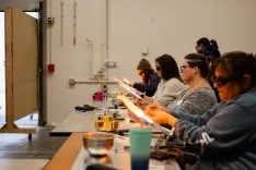 People participating in a glass blowing workshop using torches to mold and shape the glass.
