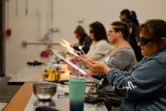 People participating in a glassblowing workshop, using torches to shape and mold glass.