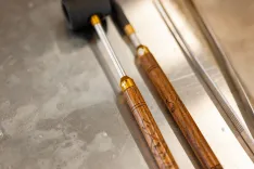 Close-up of two ornate, carved wooden wands with metal tips resting on a metal surface.