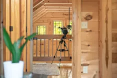 A professional camera on a tripod set up in a cozy wooden cabin interior with exposed beams and lush greenery.