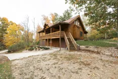 Wooden cabin with a large front porch and a garage, surrounded by trees with autumn foliage.
