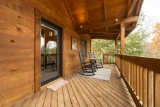 Cozy wooden cabin porch with rocking chairs overlooking a forest in autumn.