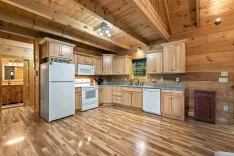 Spacious kitchen interior with wooden cabinetry and flooring, equipped with white appliances, under a vaulted wooden ceiling.