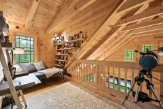 Cozy wooden loft area with a daybed, bookshelf, fluffy white rug, and a telescope by the window.