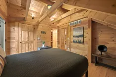 Interior of a cozy wooden cabin bedroom with a large bed, natural wood walls, exposed beams, and rustic decor.