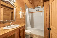 Rustic wooden bathroom interior with a white sink, large mirror, toilet, and bathtub with a white shower curtain.