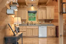 Rustic wooden kitchen interior with natural light, featuring wooden cabinets, granite countertop, a dishwasher, and a view of greenery through the window.