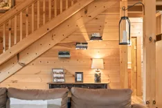 Cozy cabin interior with wooden stairs, a hanging lantern, and a side table decorated with books, a lamp, and framed photographs.