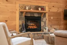 Cozy cabin living room with a stone fireplace, wooden mantelpiece with decor, and comfortable armchairs.