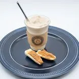 A frozen latte in a clear cup with a straw and cardboard sleeve on a blue plate with two pieces of biscotti, against a white background.