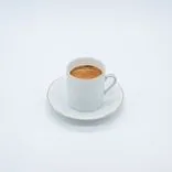 A white cup filled with espresso on a saucer, set against a white background.