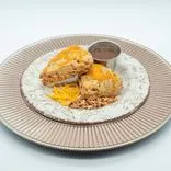 Delicious looking cheese scones with cheddar sprinkled on top and nuts around, served on a decorative plate with a side of sauce.
