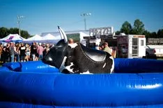  Mechanical bull riding setup at an outdoor event with people gathered in the background.