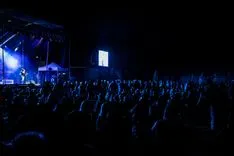 Crowd of people at a nighttime outdoor concert with stage lights.