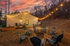 Outdoor backyard gathering area with string lights, a fire pit, and chairs at dusk with a colorful sky.