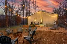 Outdoor backyard setting at twilight with string lights, a fire pit surrounded by chairs, a hot tub, and a modern shed with a deck.
