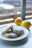 Lemon cookies with white icing and zest on a plate, with whole lemons in the background near a sunny window.