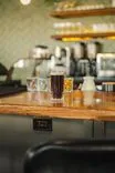 A glass of dark beer on a wooden bar counter with blurred background of a coffee machine and various bar paraphernalia.