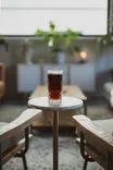 A glass of dark beer with a frothy head on a round table in a cozy room with plants and warm lighting.