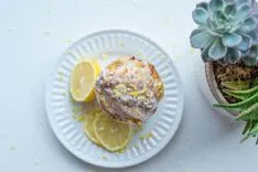 Lemon-glazed muffin on a white plate beside sliced lemons and a succulent plant.