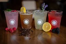Four specialty drinks in branded glasses, garnished with fresh fruits and coffee beans on a wooden table.