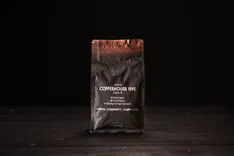 A sealed bag of Coffeehouse Five coffee on a dark wooden surface with text indicating the brand supports community initiatives.