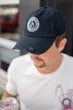 Close-up of a person wearing a navy blue baseball cap with a coffeehouse logo, slightly looking down with a blurred background.