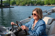 Woman smiling while steering a boat on the water.