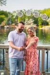 A happy couple embracing at an outdoor baby shower with decorations that say "Baby Shower" in the background.
