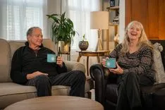 Elderly couple laughing and enjoying coffee together in a cozy living room setting.