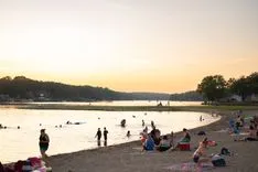 People enjoying a sunset at a beach with swimmers in the water and others relaxing on the sand.