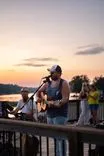 Band performing outdoors on a deck at sunset with water in the background.