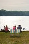 Group of people sitting by a lakeside with chairs and a cooler, enjoying the view.