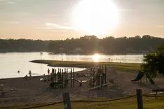 Sunset over a tranquil lake with a playground silhouette and a pier extending into the water.