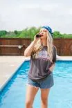 Woman in a bandana and casual clothes drinking from a bottle by the poolside.