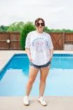 Woman in sunglasses and casual summer outfit standing by a swimming pool.